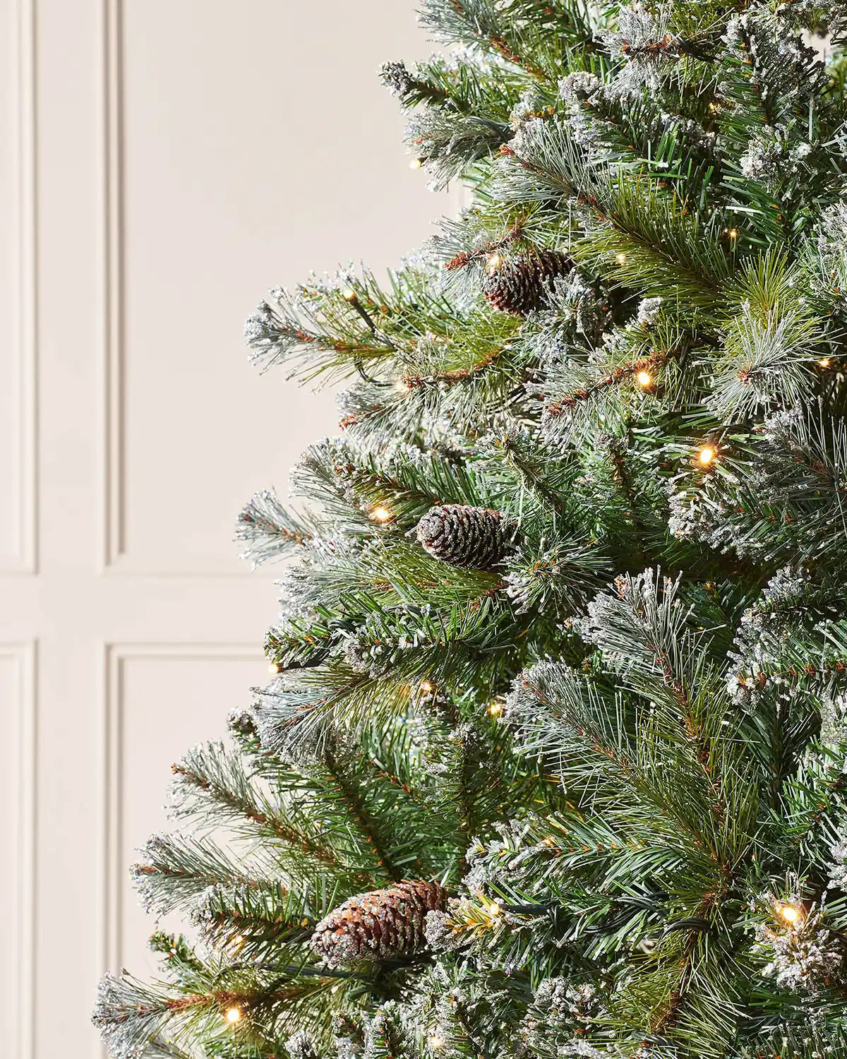 Close-up of Blue Brockton spruce branches with frosted pinecones and warm white LED lights.