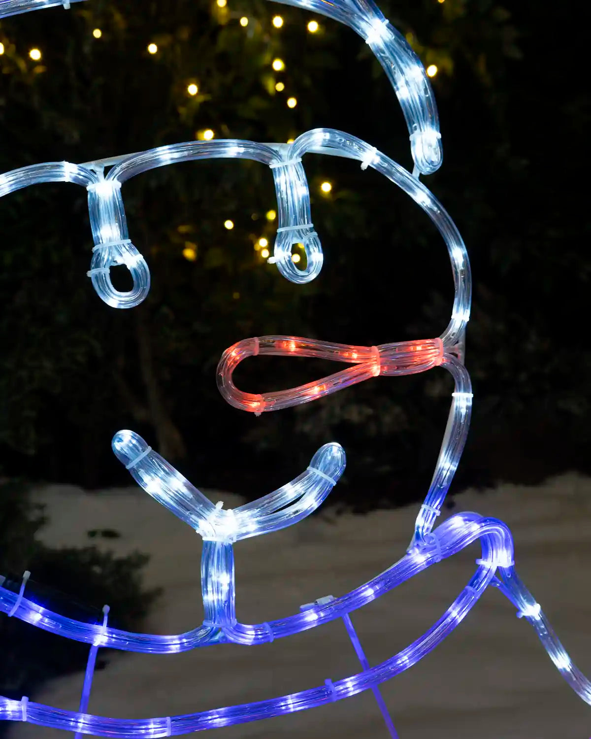 Close-up of an illuminated snowman face with white, red and blue rope lights.