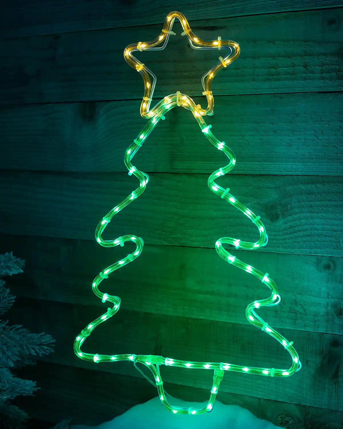 Pre-lit Christmas tree rope light displayed on a wooden wall at night