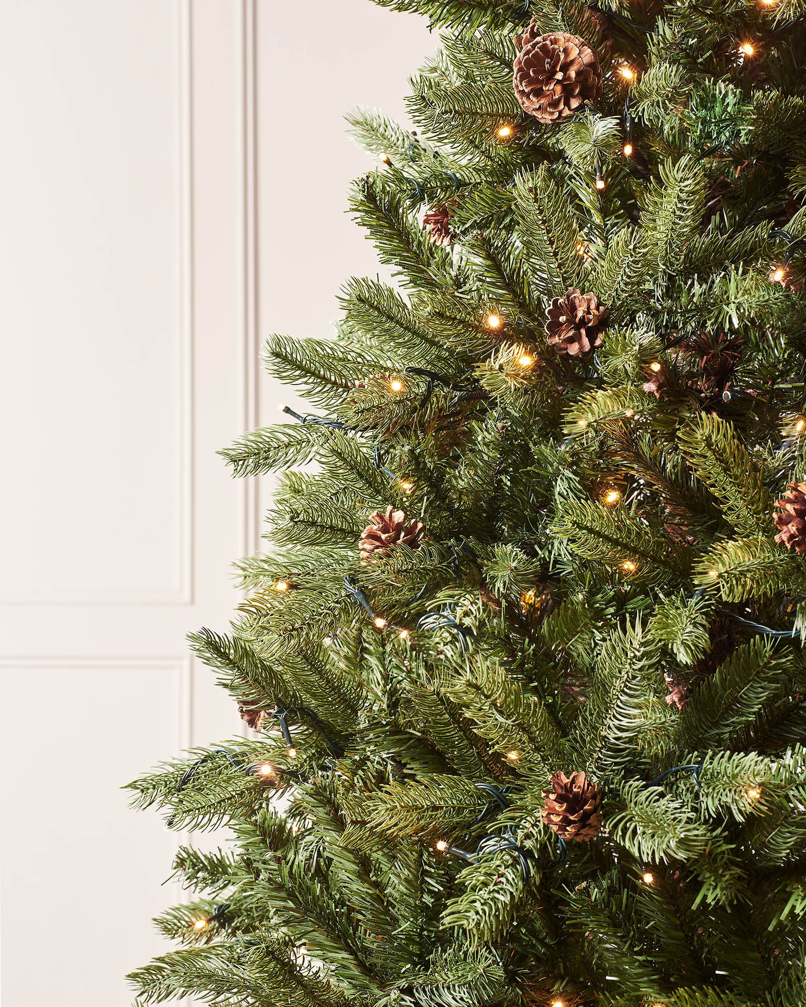 Close-up of Craford Pine branches with pinecones, warm white lights and layered green foliage.