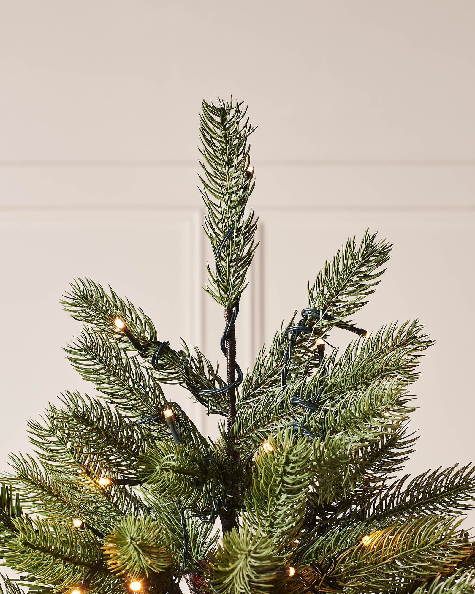 Close-up of the top section of the Craford Pine Christmas tree with warm white lights and wall panelling in the background.