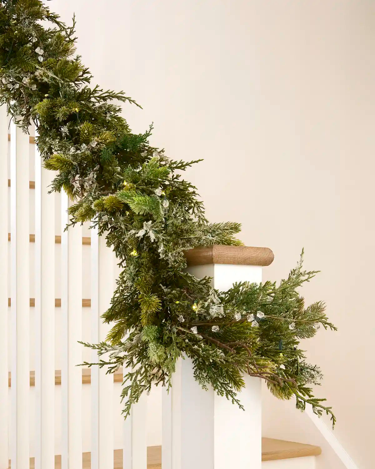 Decorative snow flocked garland with warm white lights and mixed foliage wrapped around a staircase bannister.