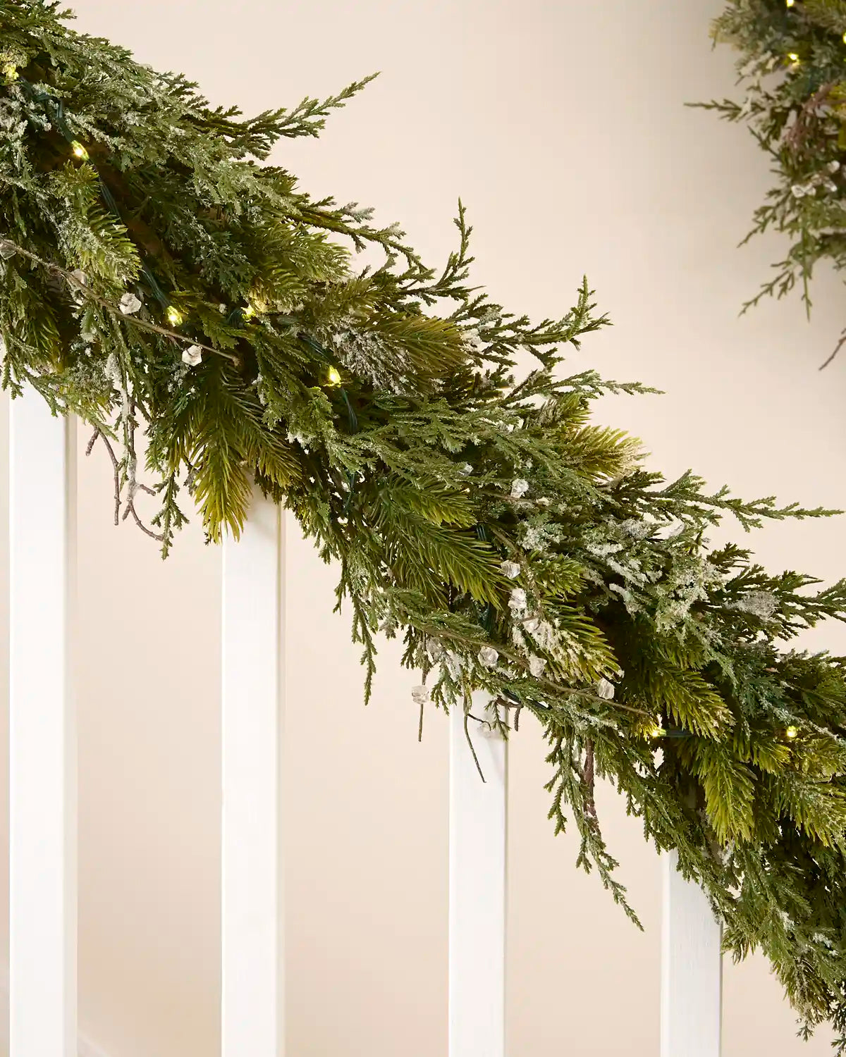 Pre-lit 9 ft decorative snow flocked garland with mixed green foliage and warm white lights on a staircase.