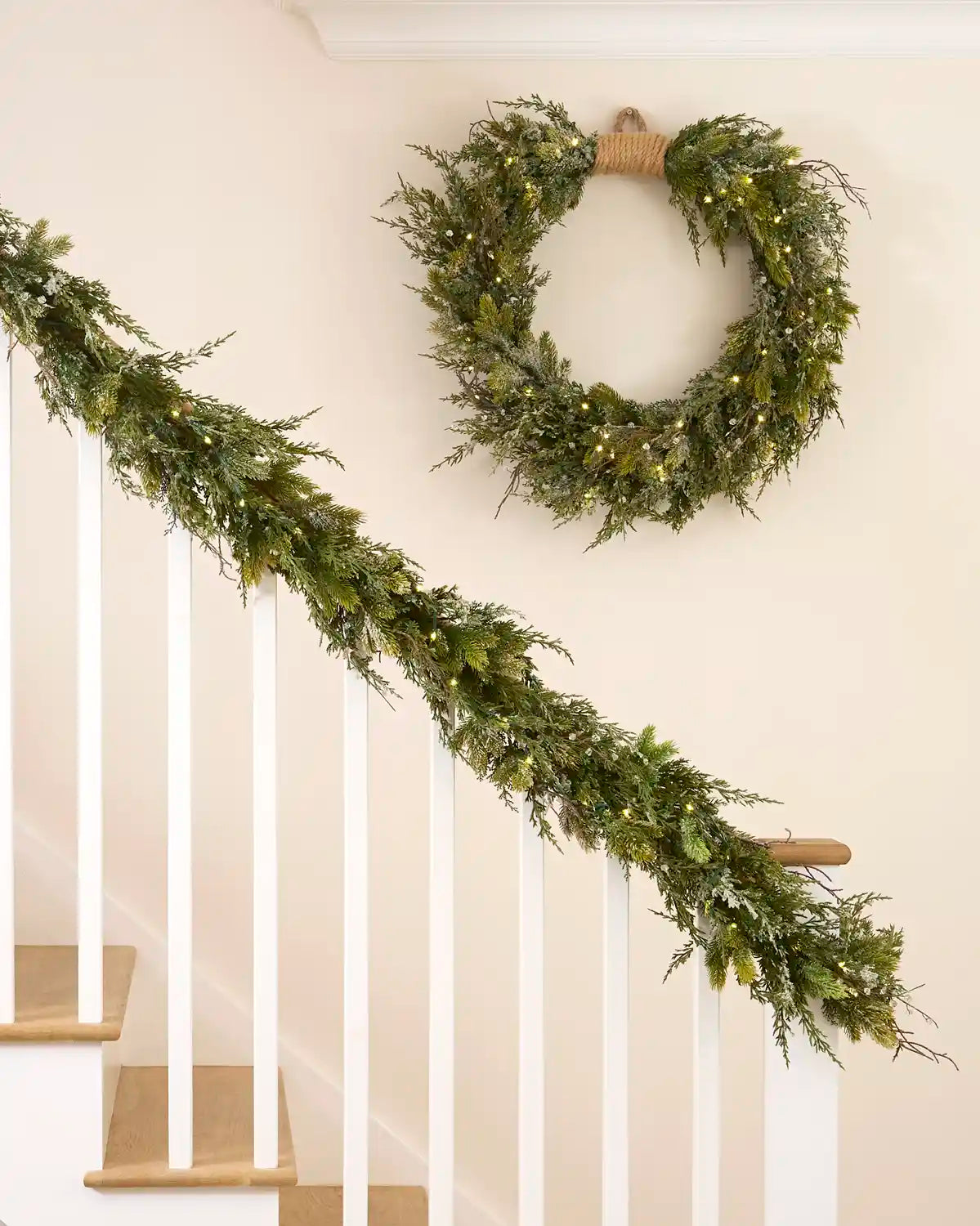Pre-lit snow flocked garland styled along a staircase with a matching decorative wreath.