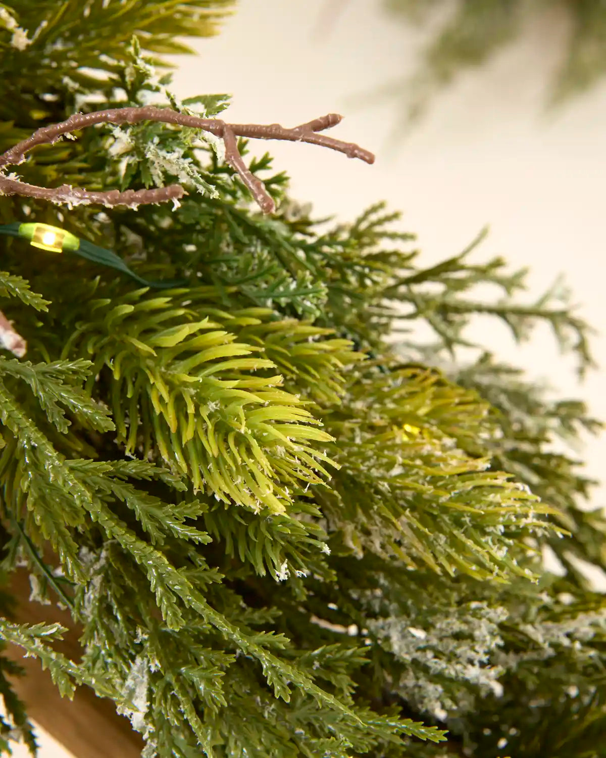 Close-up of mixed green foliage, snow flocking, decorative twigs and warm white lights on the garland.