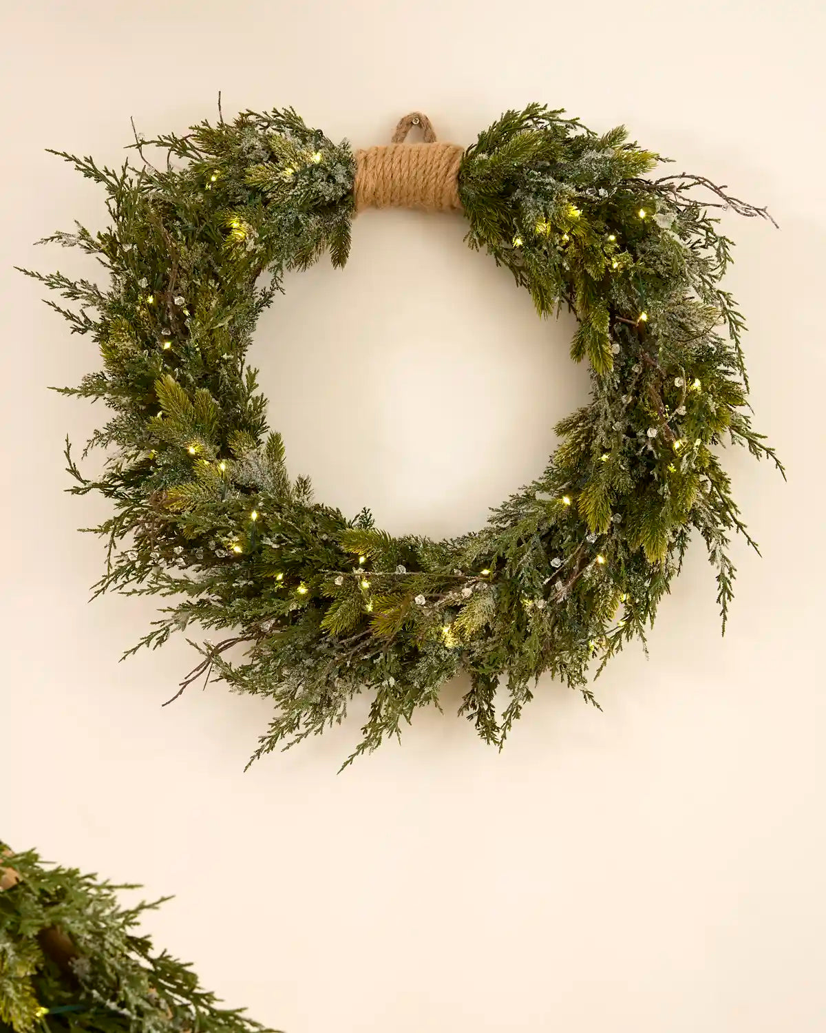 Pre-lit 76 cm decorative snow flocked wreath with mixed green foliage and warm white lights.