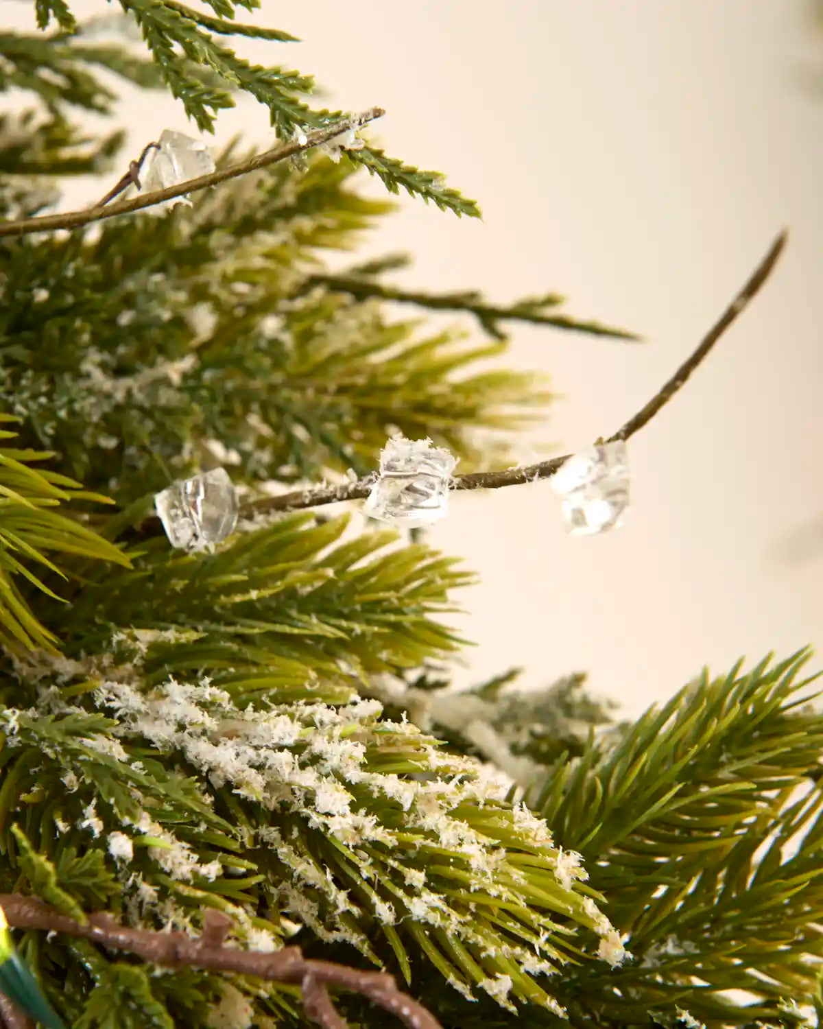 Close-up of clear crystal-style decorations among snow flocked foliage on the pre-lit wreath.