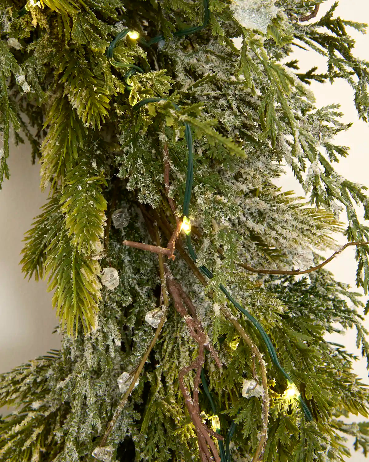 Close-up of warm white lights woven through snow flocked green foliage and decorative twigs.