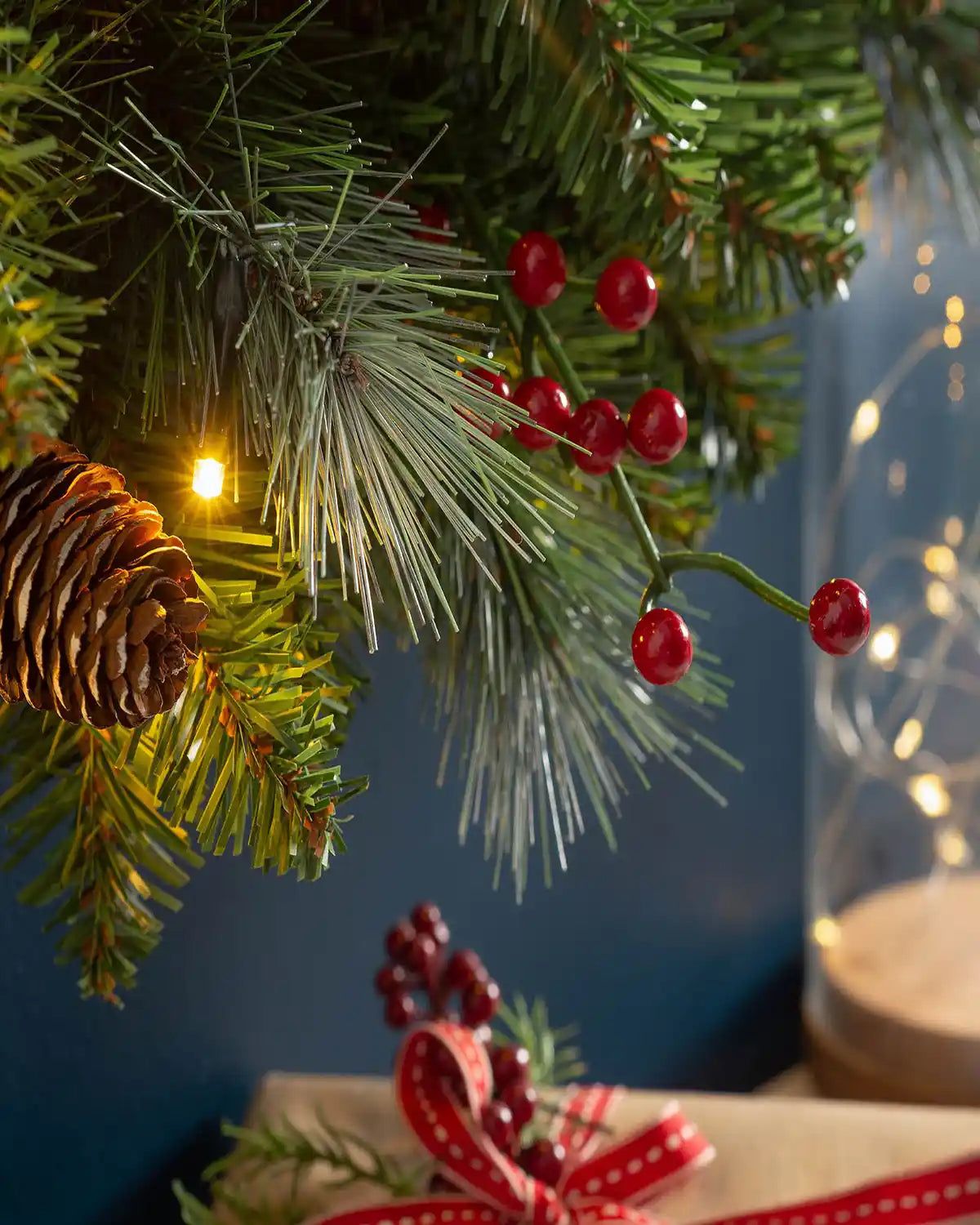 Close-up of red berries, frosted foliage, pinecones and warm white lights on a 60 cm Christmas wreath