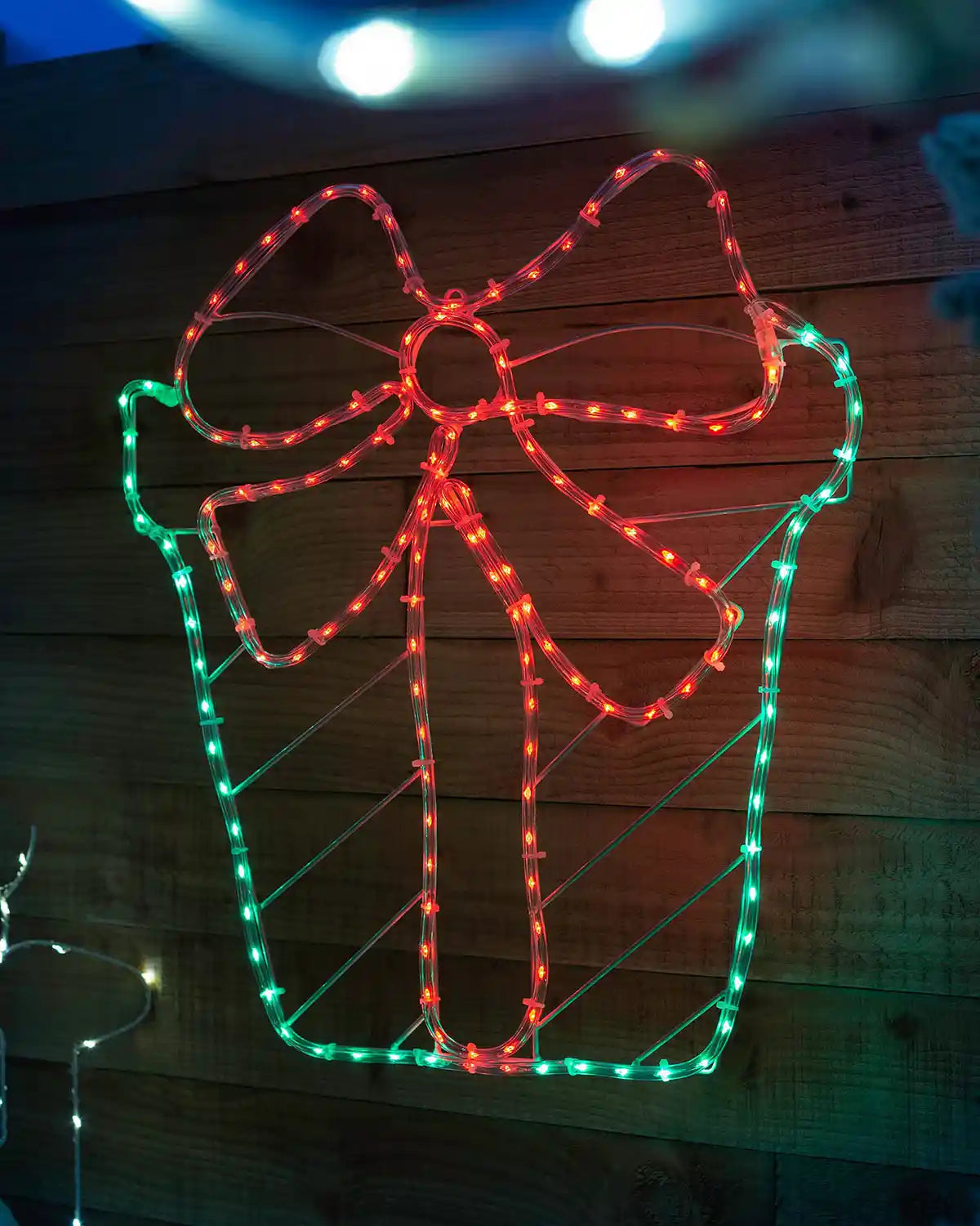 Pre-lit giftbox rope light displayed on a wooden wall at night
