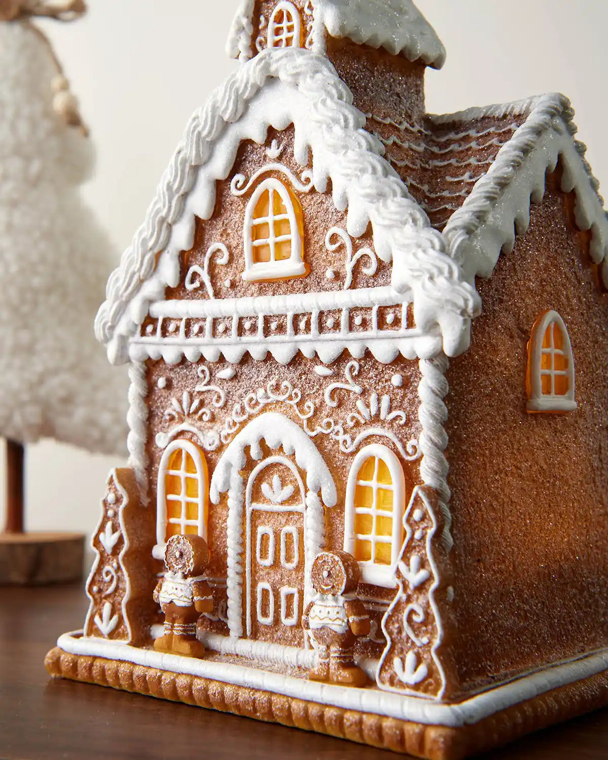 Close-up of the pre-lit gingerbread house showing the front windows, door, icing-style trim and snowy roof detail.