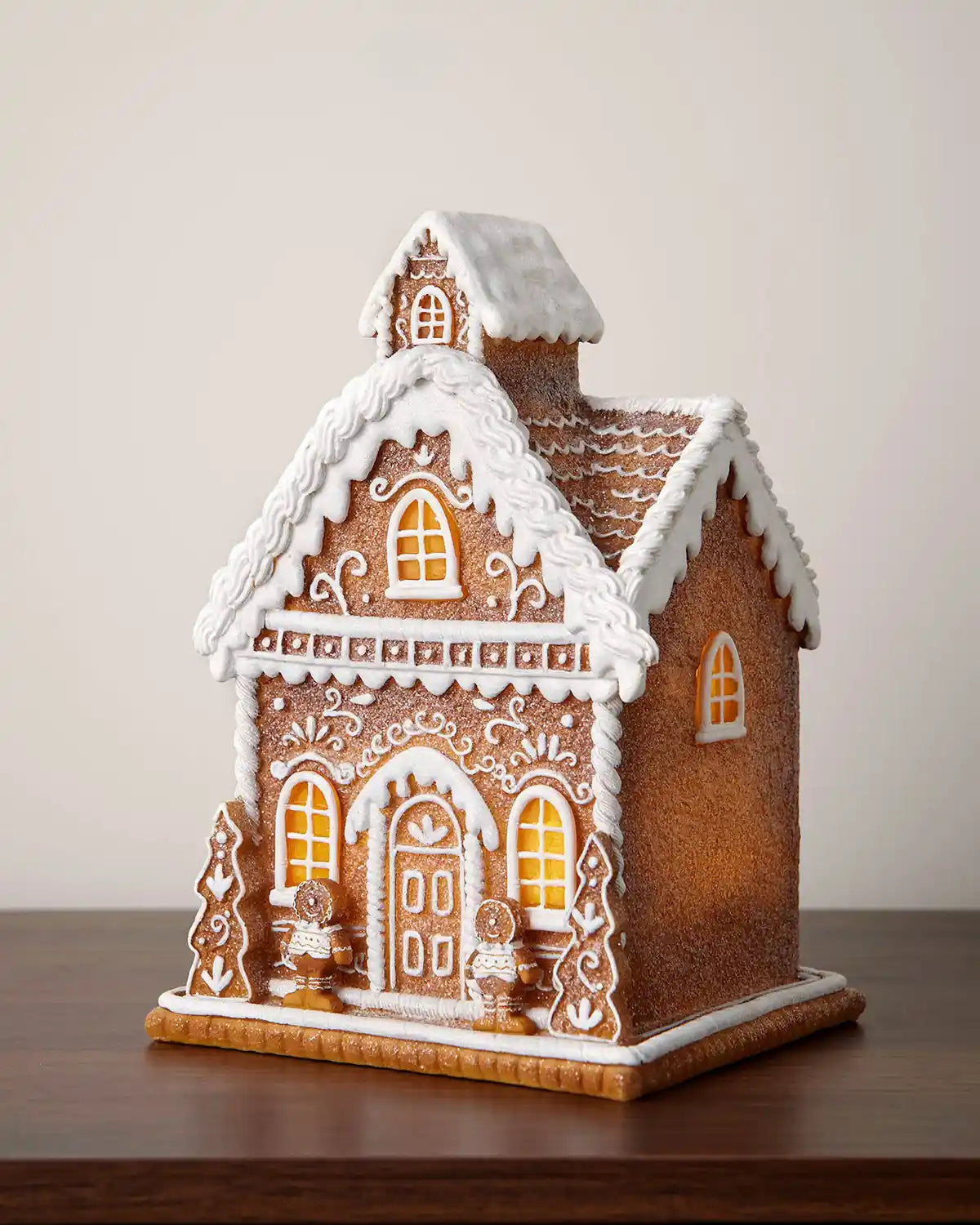 22cm pre-lit gingerbread house decoration with icing-style details, snowy roof and glowing windows on a wooden table.