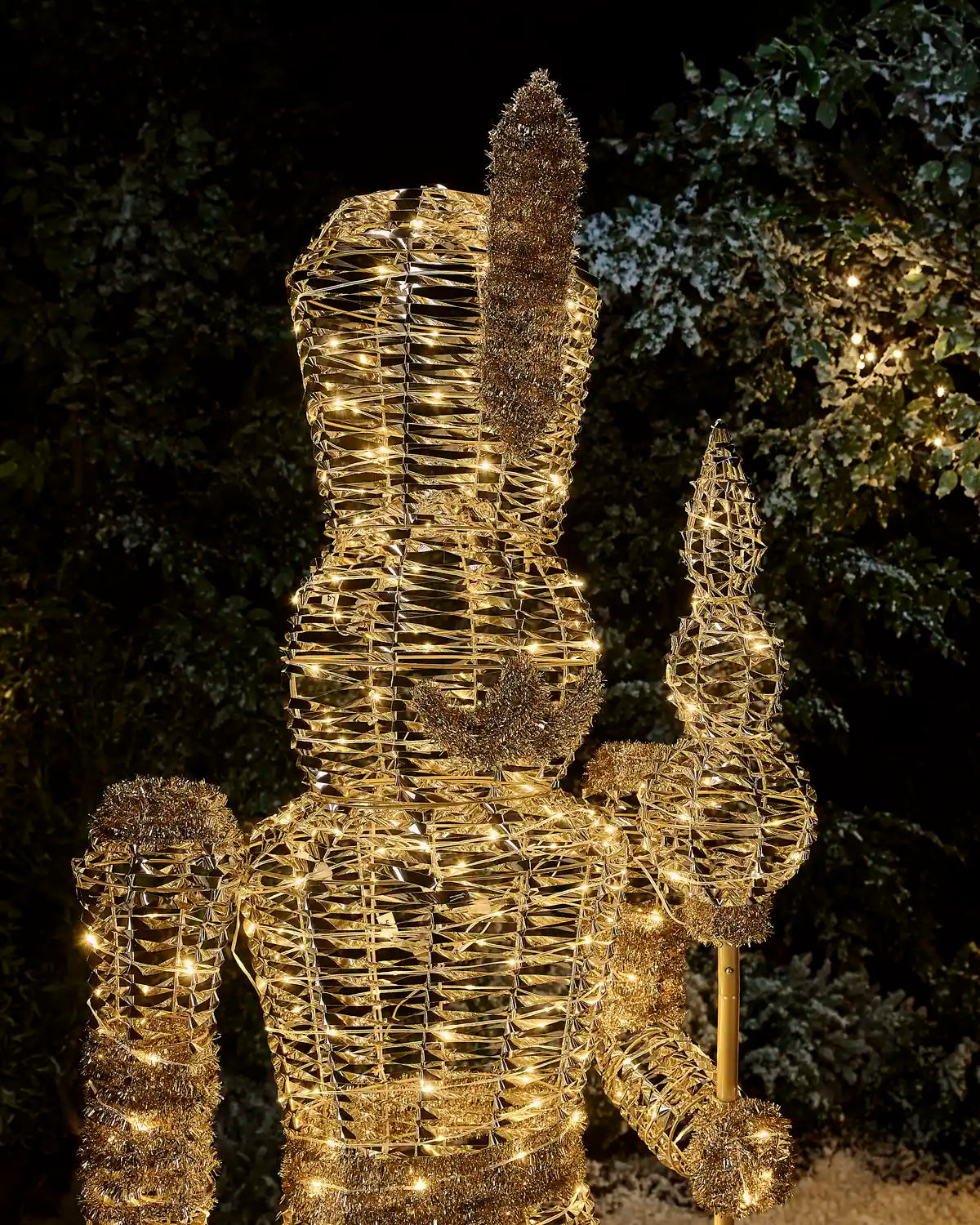 Close-up of the illuminated gold nutcracker showing its feathered hat, moustache, uniform and decorative staff.