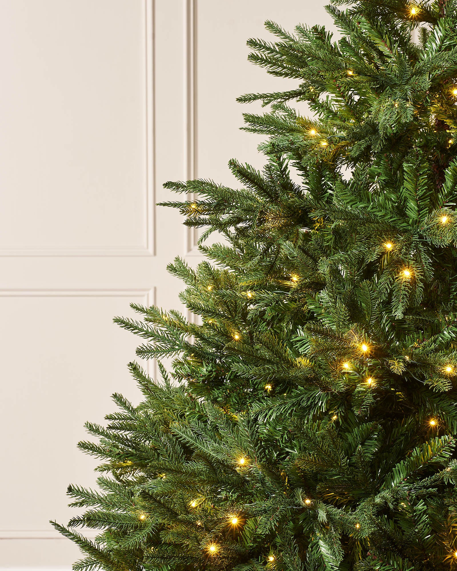 Close-up of dense green Nordmann fir branches with warm white LED lights.