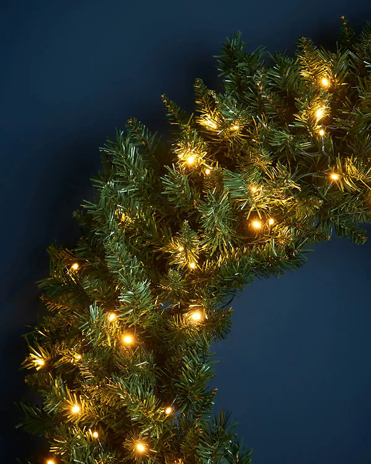 Detail view of green wreath foliage illuminated with warm white LED lights