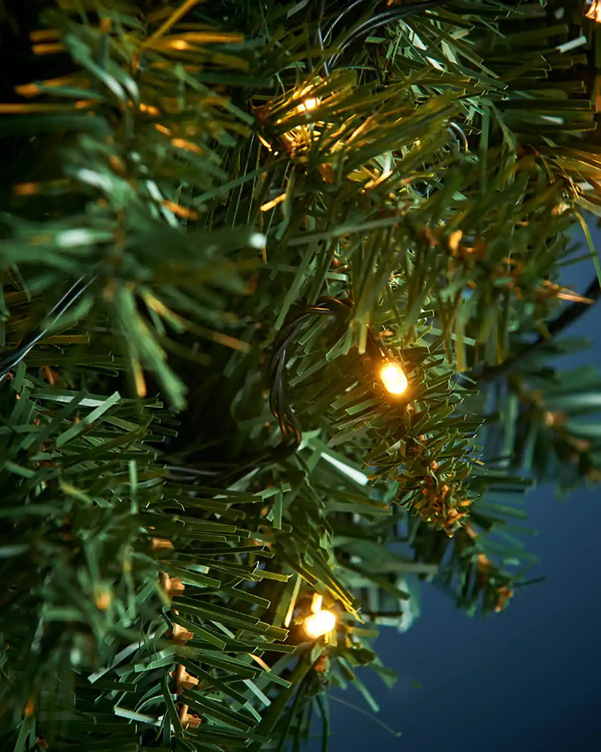 Person arranging a 1 m pre-lit majestic Christmas wreath on a blue wall