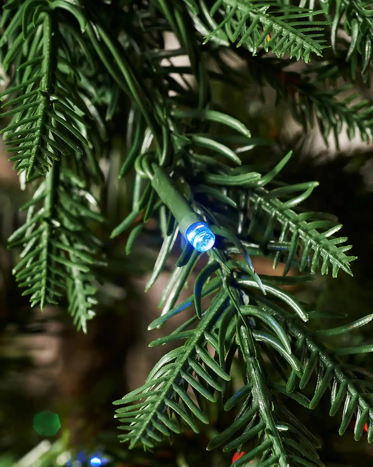 Close-up of a blue LED light nestled among green mixed pine branches on the Pre-Lit Mixed Pine Natural Bark Christmas Tree.