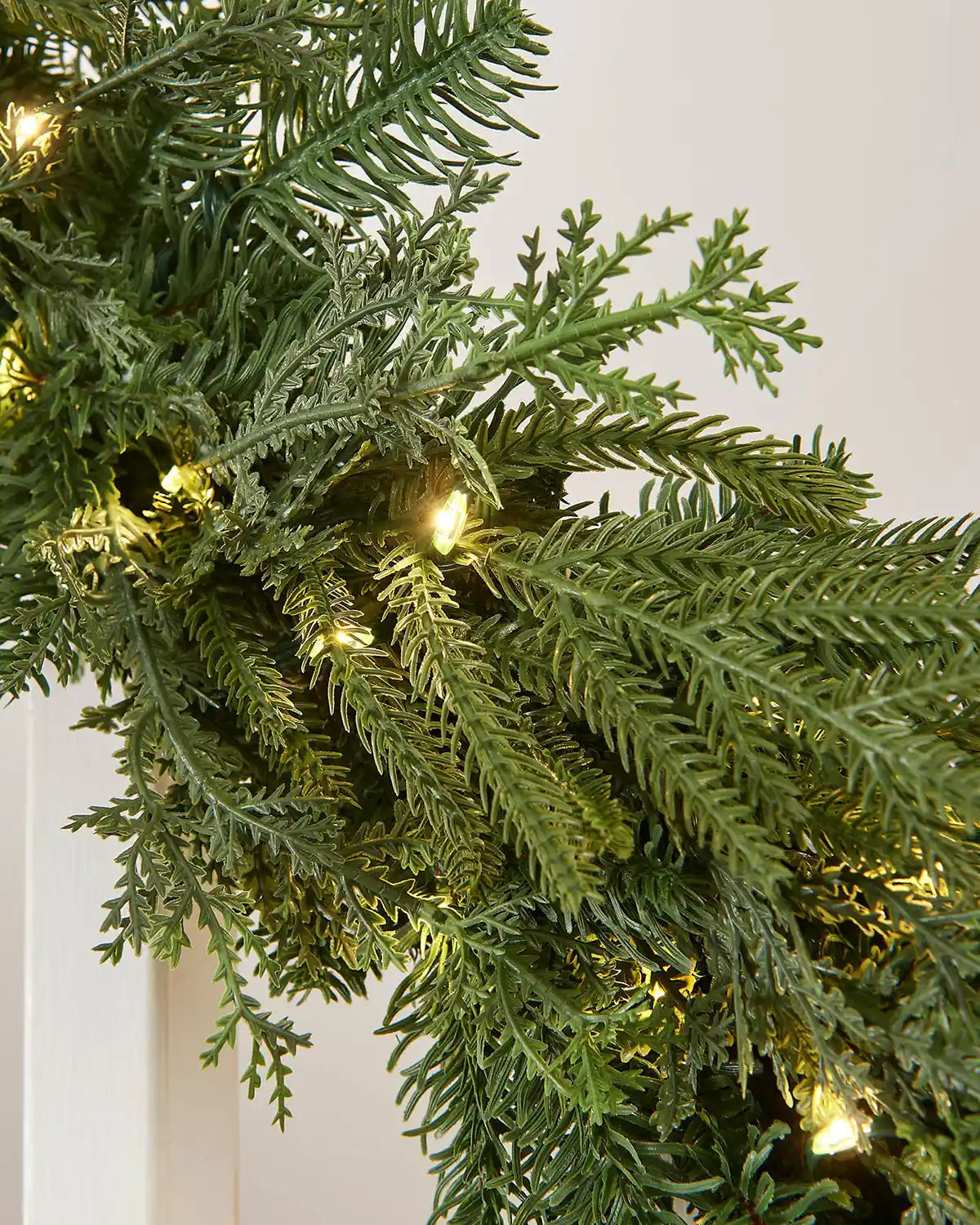 Close-up of natural fir garland foliage with mixed greenery and warm white LED lights.