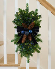 Pre-lit 60 cm navy Christmas garland swag with berries, pinecones, baubles and velvet bow.