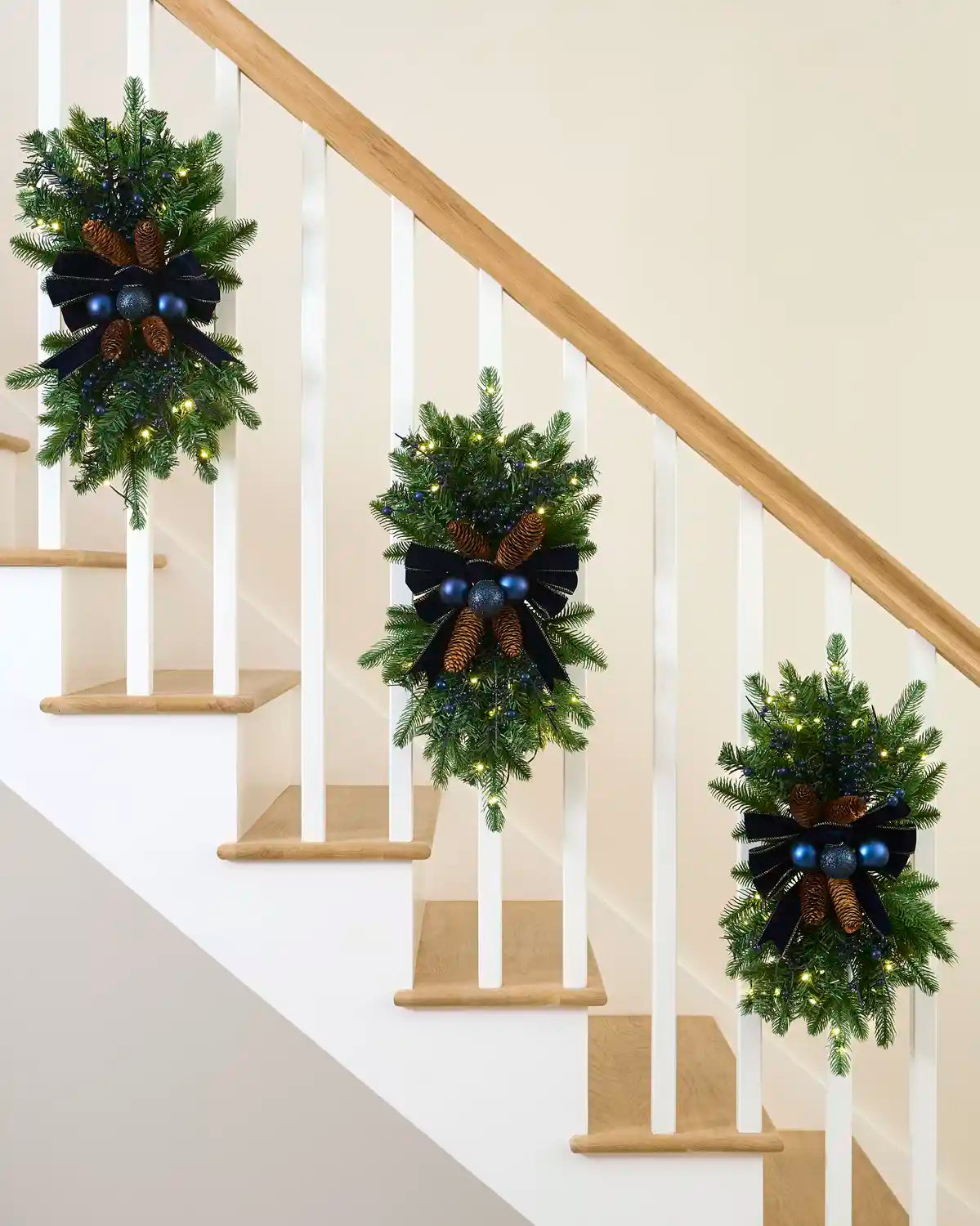Three pre-lit navy garland swags displayed along a staircase banister.