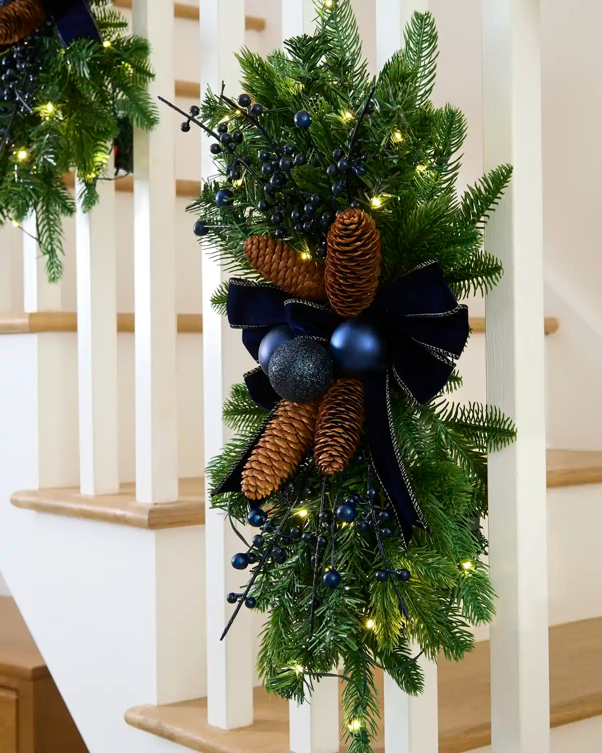 Navy pre-lit garland swag with warm white lights displayed on a staircase.