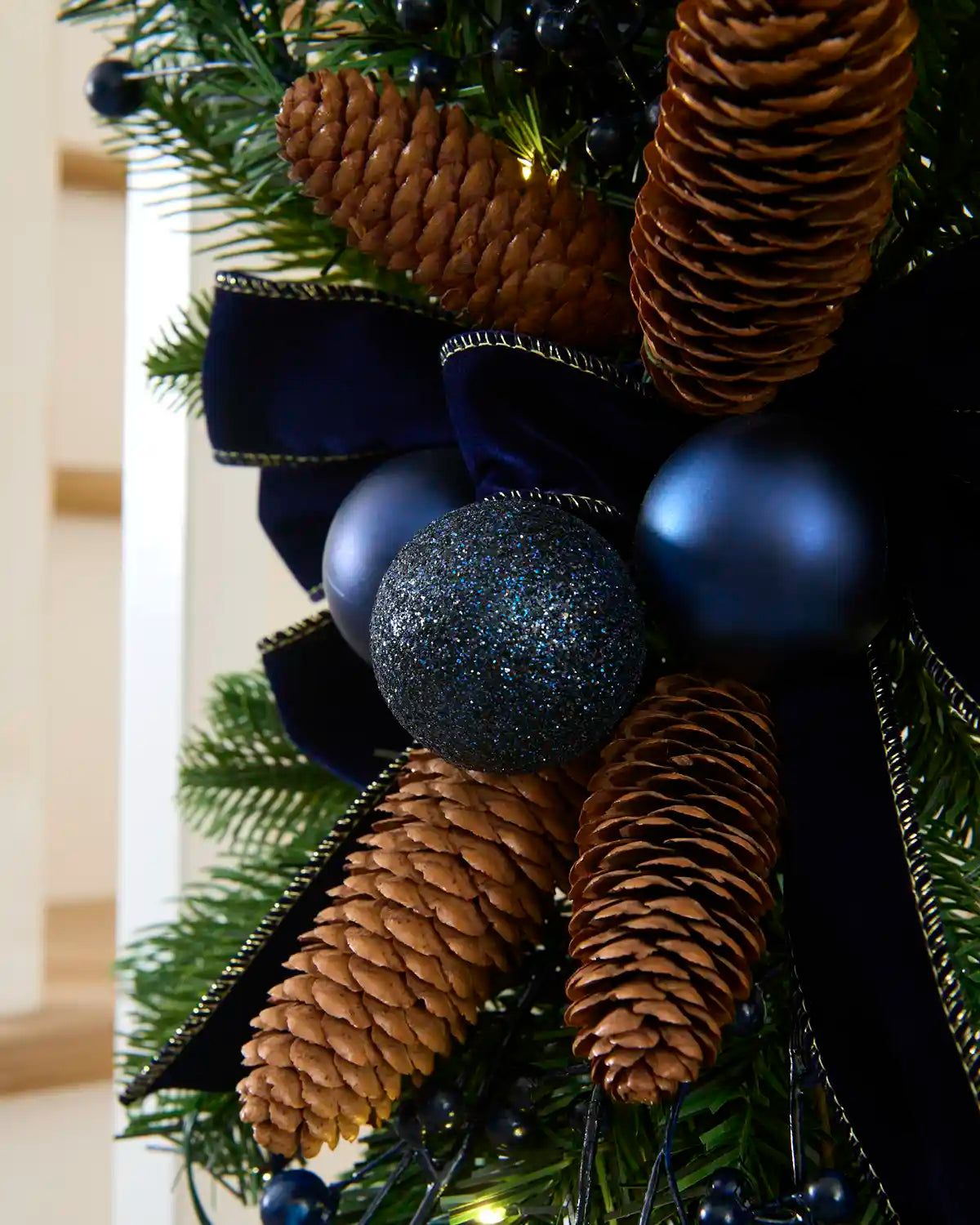 Close-up of navy velvet bow, blue baubles and natural pinecones on the garland swag.