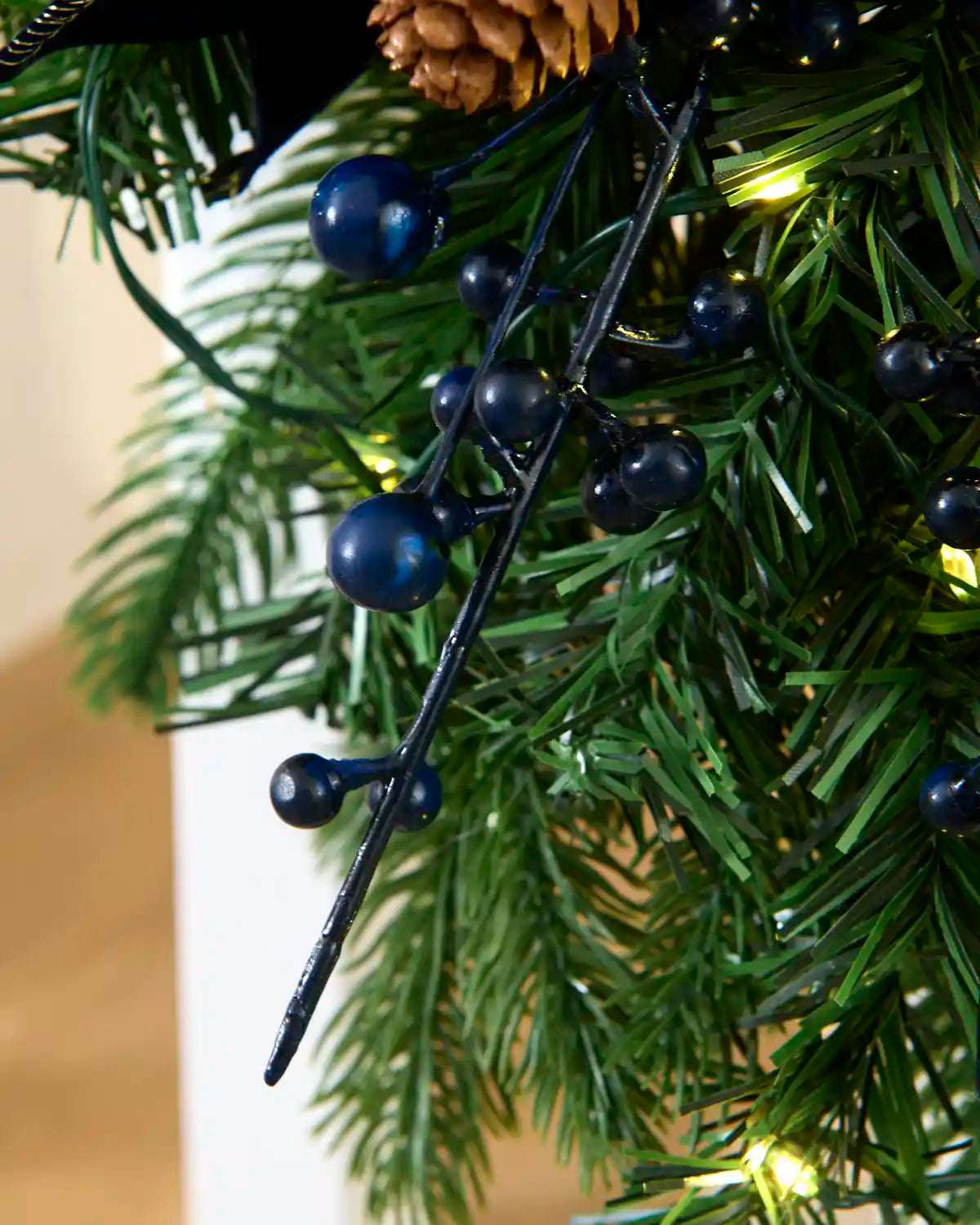 Close-up of navy berry picks, green foliage and warm white lights on the garland swag.