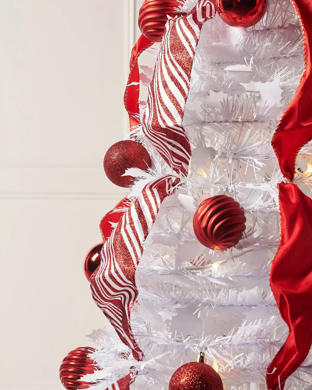 Close-up of red baubles and striped ribbon on a white pre-lit pop-up Christmas tree