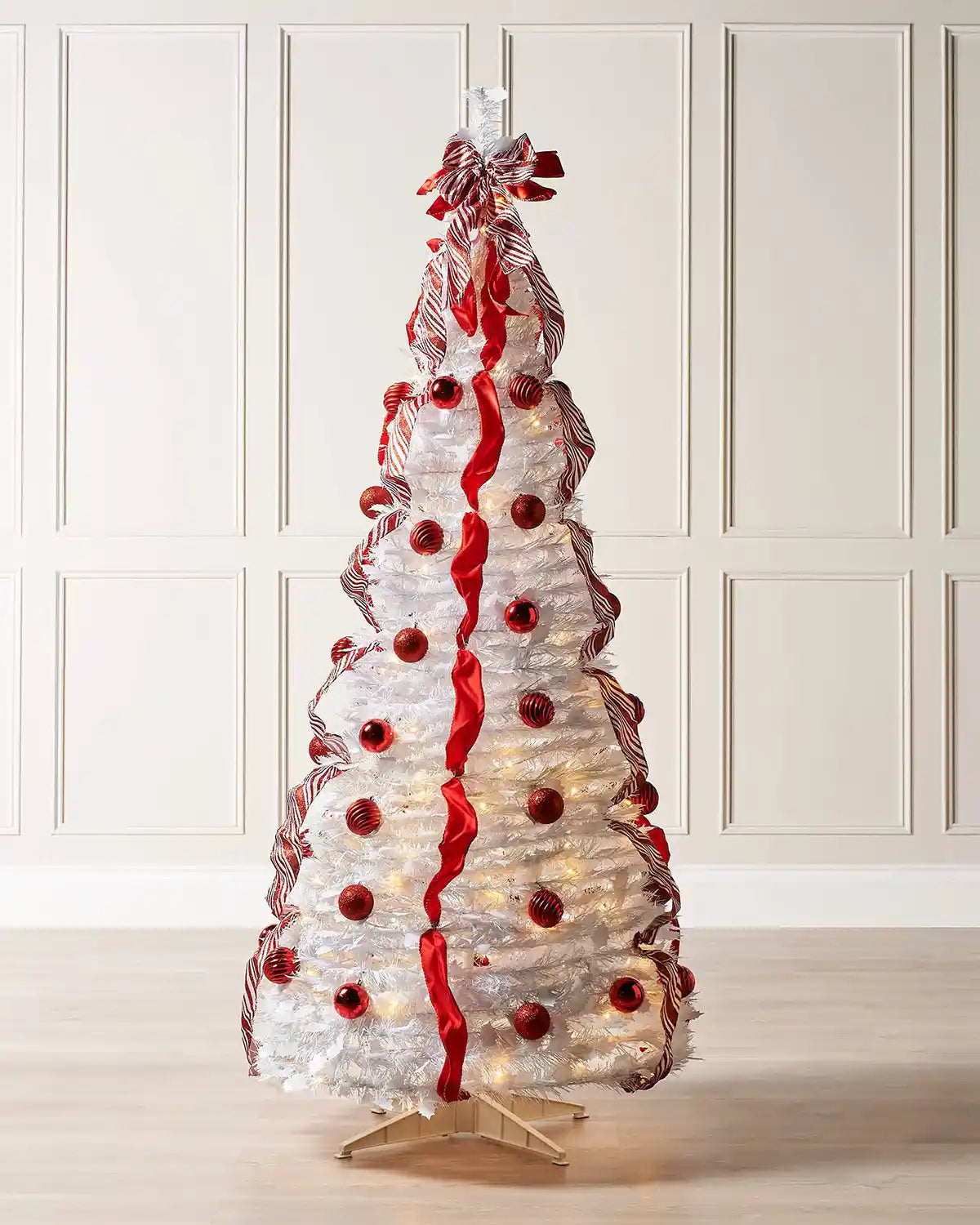 Pre-lit red and white pop-up Christmas tree displayed in a room with warm white LED lights