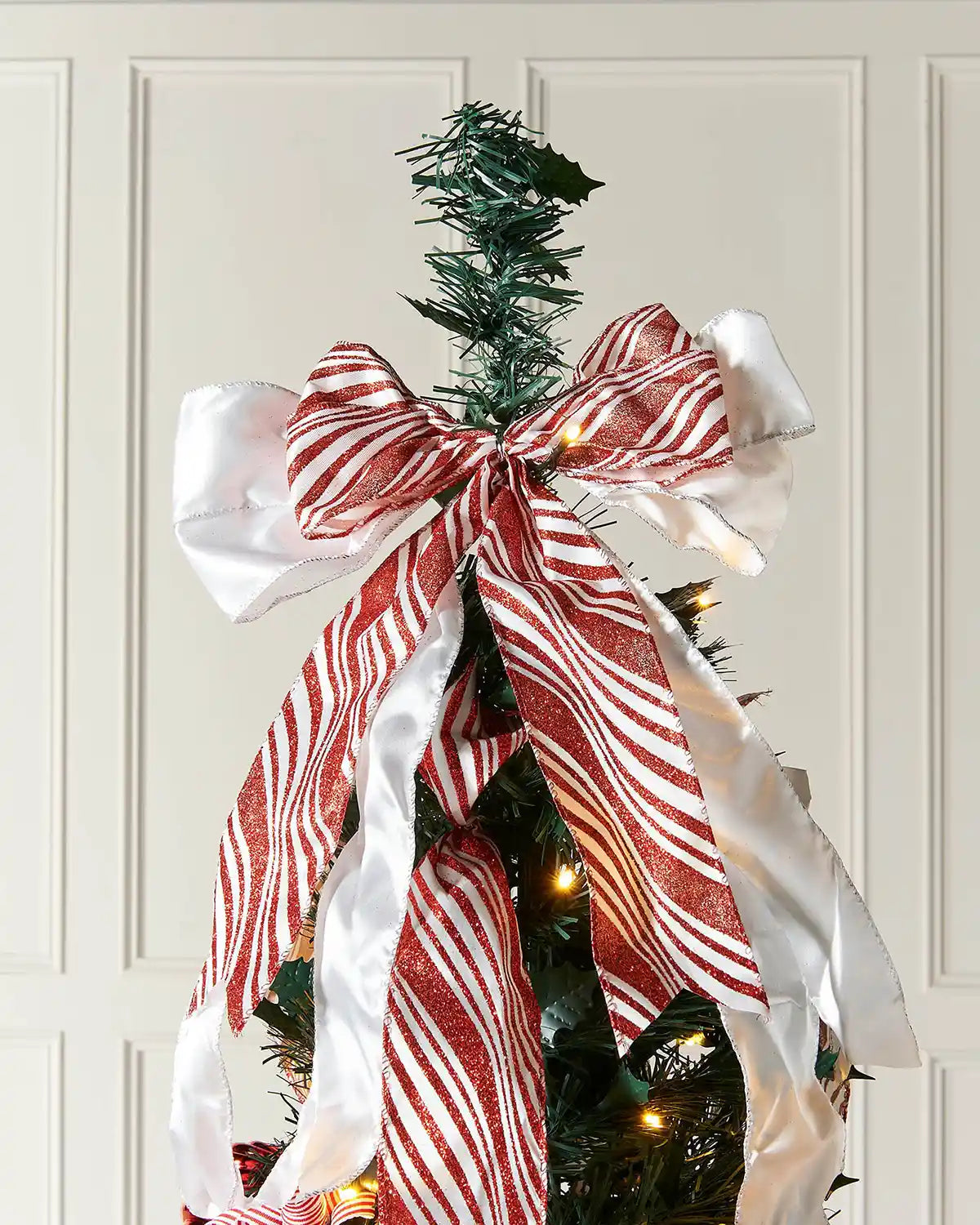 Close-up of the red and white bow topper on the green pre-lit pop-up decorated Christmas tree