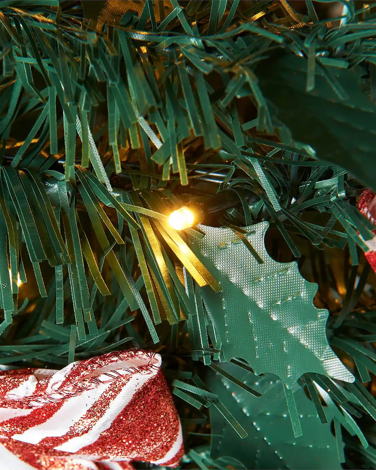 Close-up of warm white LED light and green PVC foliage on the red and white decorated pop-up Christmas tree