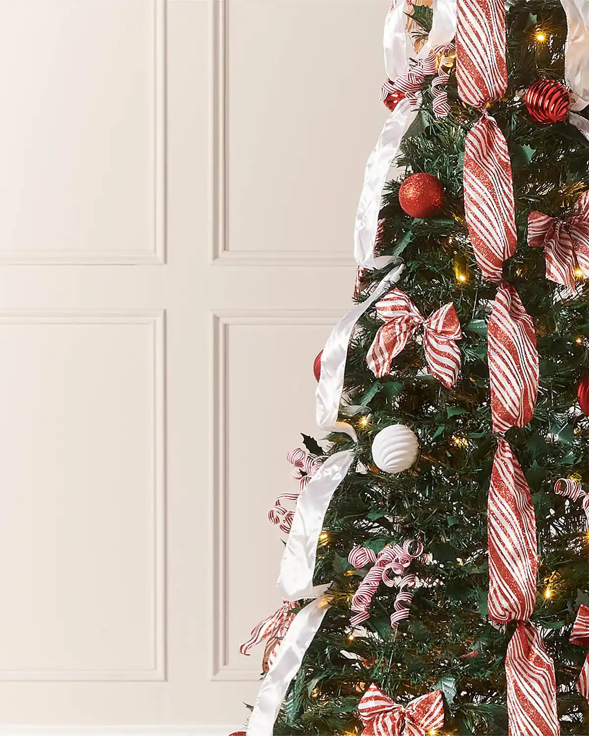 Close-up of red and white striped ribbon, baubles and warm white lights on the green pop-up Christmas tree