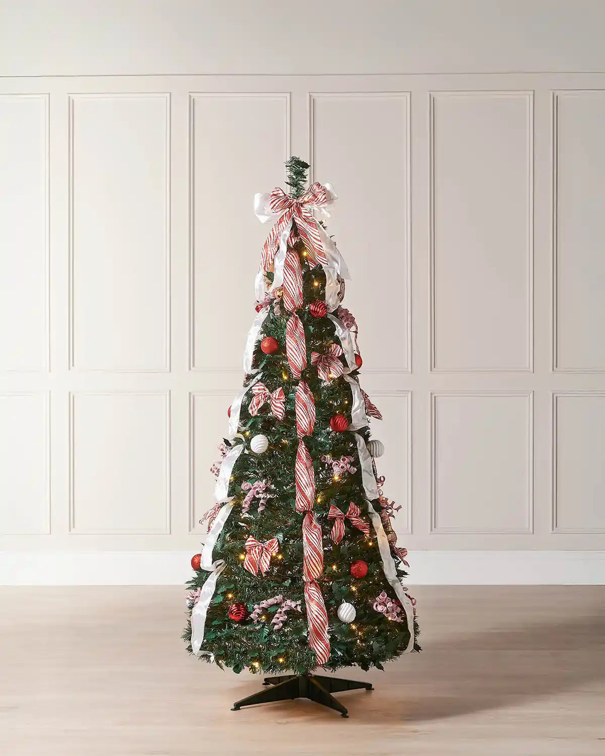 Pre-lit green pop-up decorated Christmas tree with red and white ribbon displayed in a room