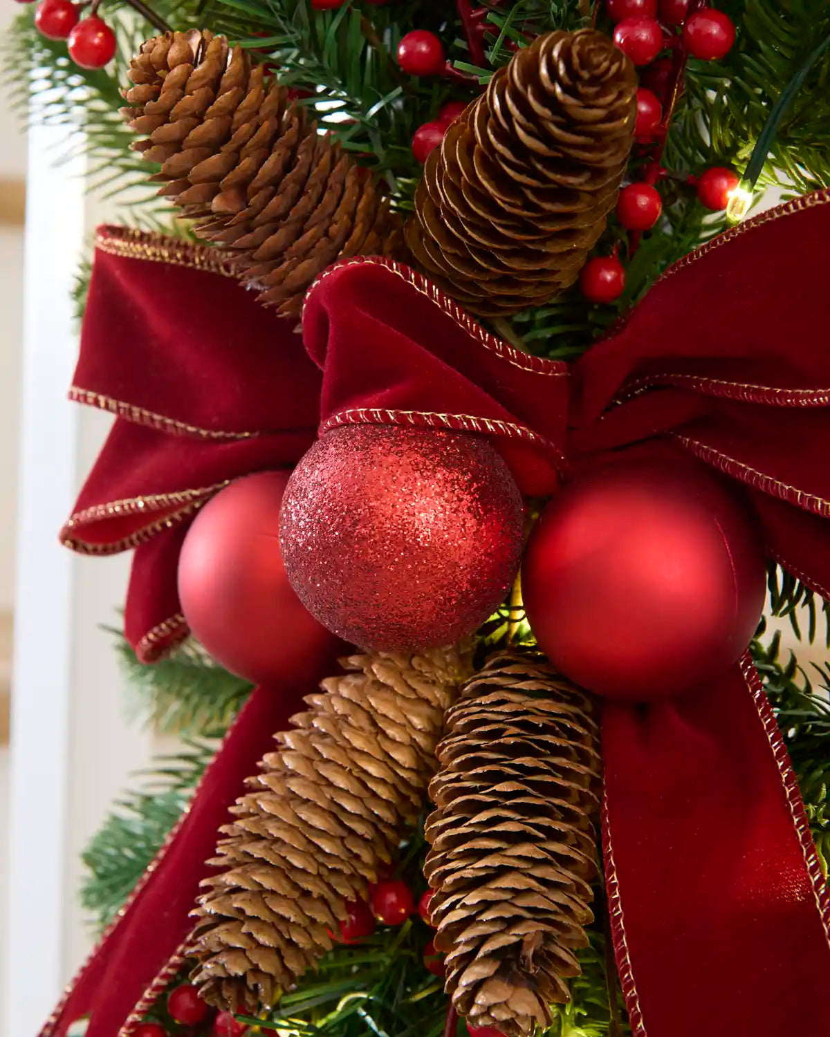 Close-up of burgundy velvet bow, red baubles and natural pinecones on the garland swag.