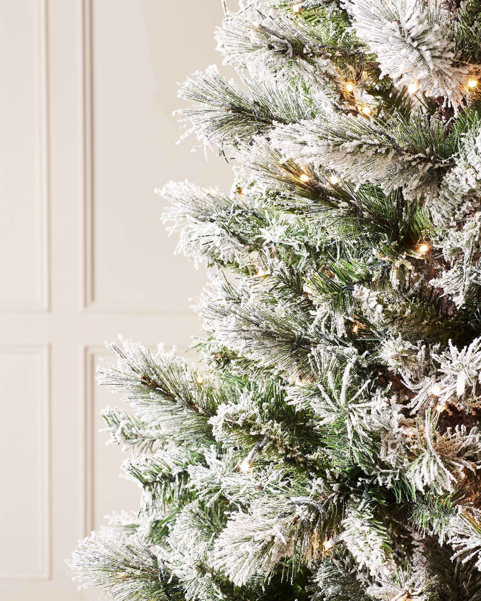 Close-up of snow flocked spruce branches with warm white lights and mixed green foliage.