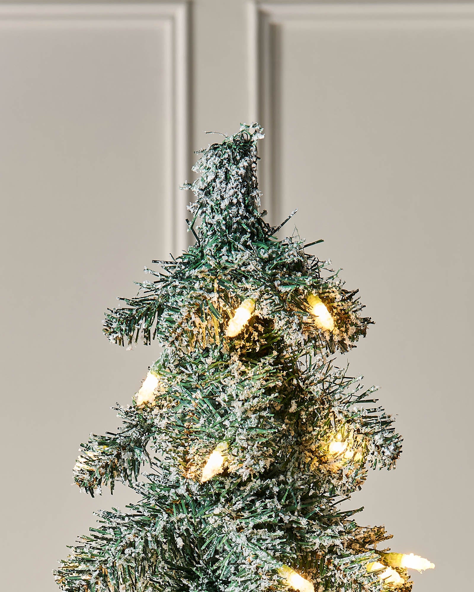 Top section of the 6.5ft snow-flocked alpine Christmas tree with warm white lights.