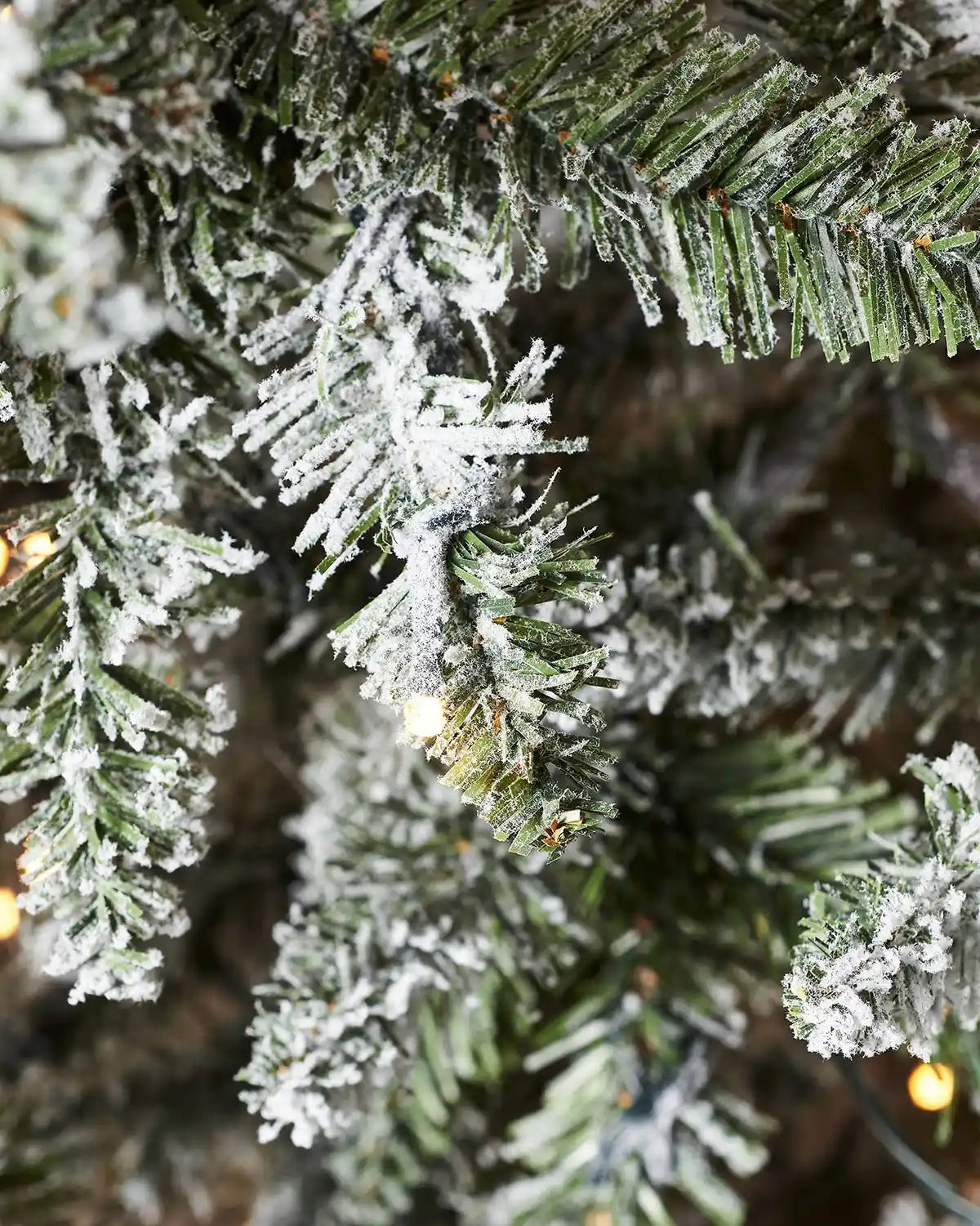 Detailed close-up of green PVC branch tips covered in white flocking with warm white lights visible between the branches.