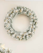 Pre-lit 76 cm snow flocked Christmas wreath with warm white LED lights displayed on a wall.