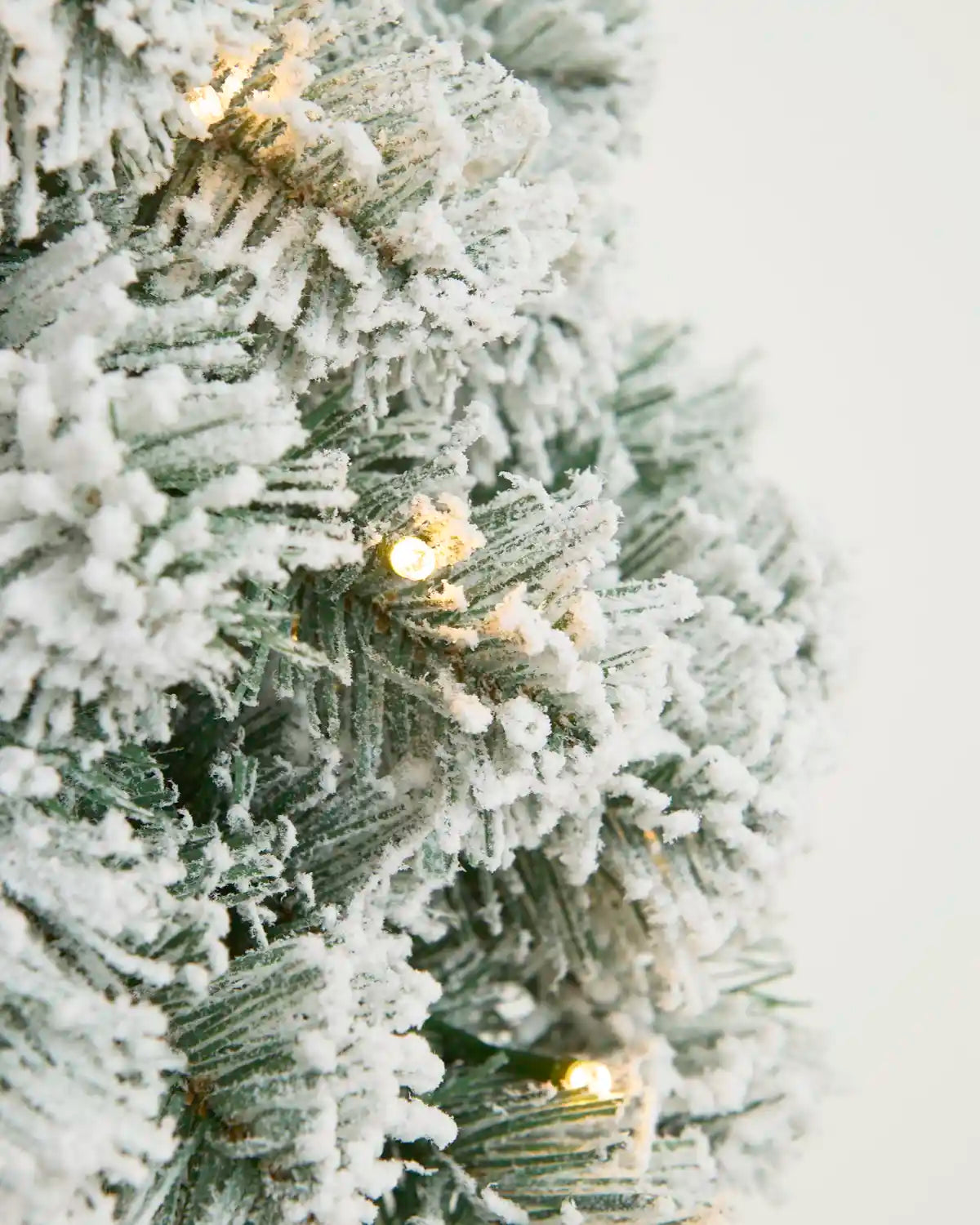 Close-up of warm white LED lights nestled among heavily snow flocked wreath foliage.