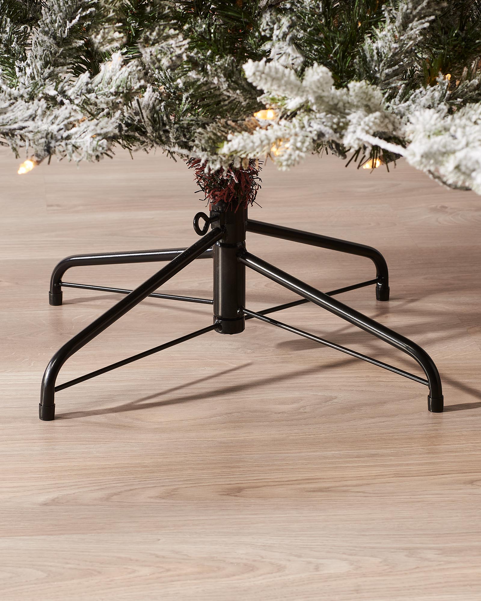 Close-up of the black metal tree stand beneath a snow flocked Fraser fir Christmas tree.