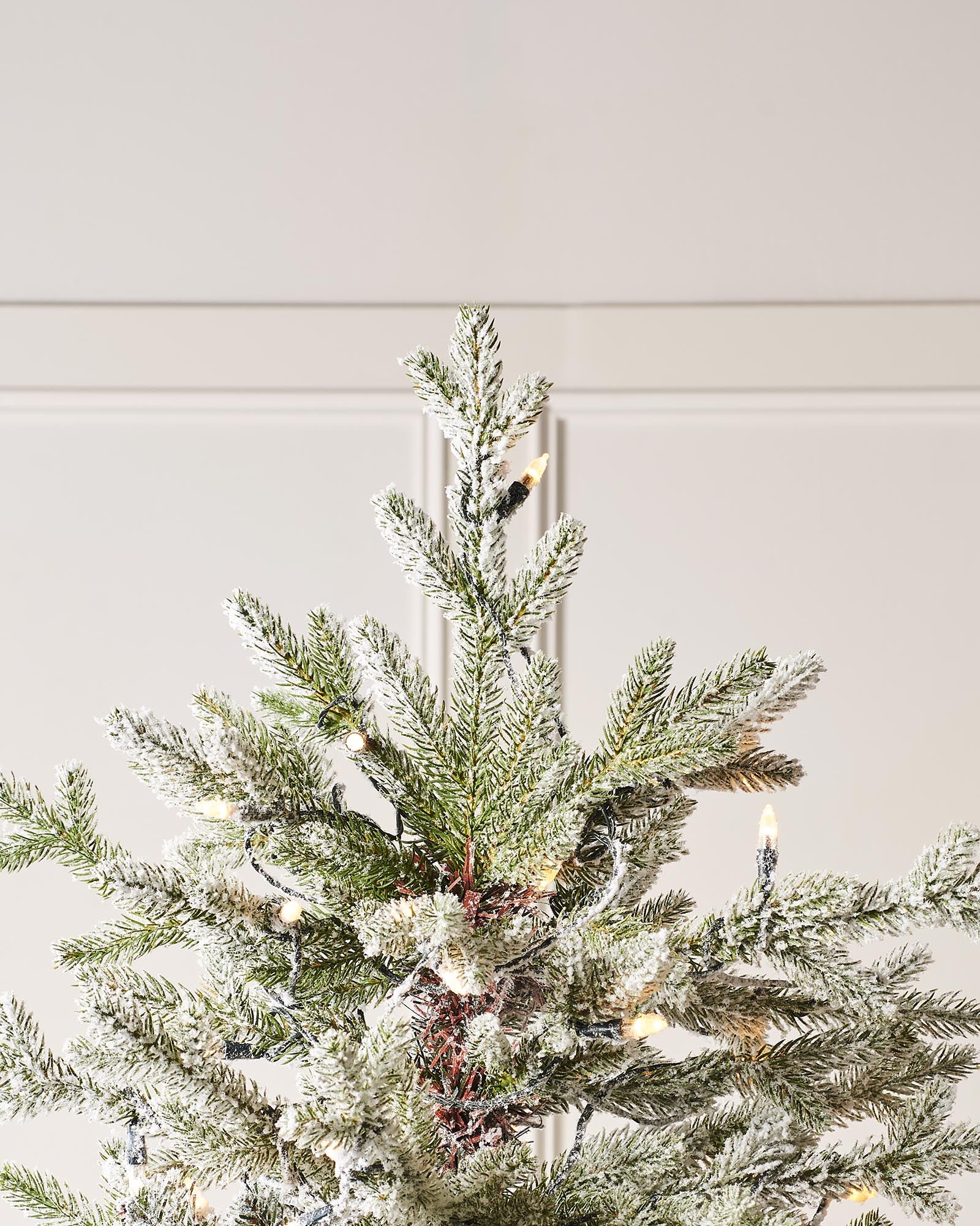Top section of a snow flocked Fraser fir Christmas tree with warm white candle-style lights.