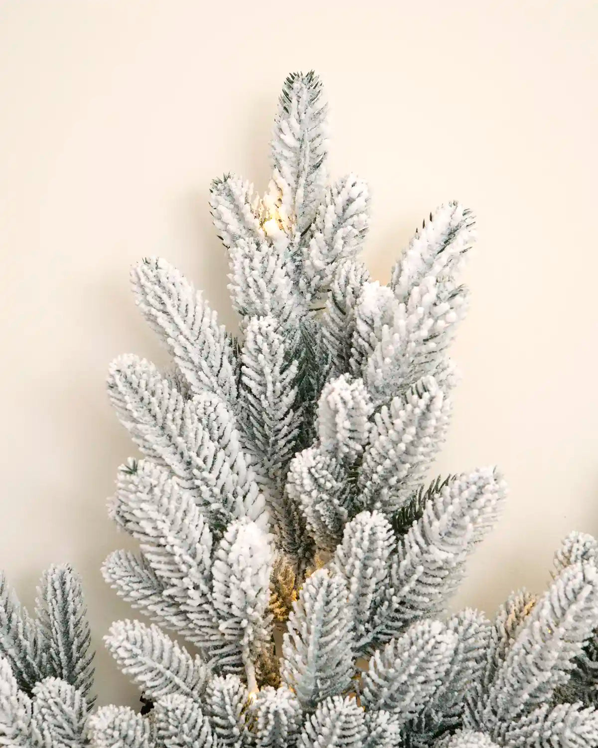Close-up of one point of the snowflake wreath showing densely snow-flocked PE foliage and warm white LEDs.