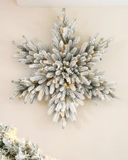 Pre-lit 80 cm snow-flocked snowflake wreath with dense frosted foliage and warm white LED lights displayed on a wall.