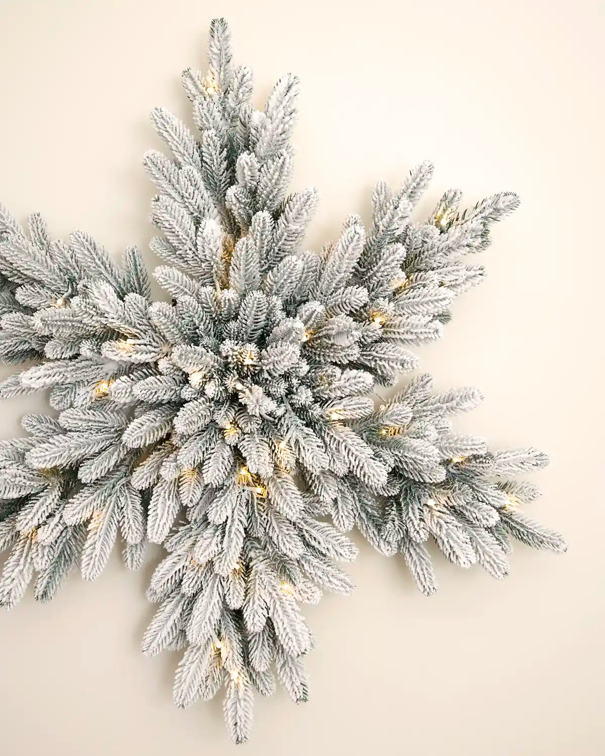 Angled view of the 80 cm snowflake wreath showing snow-flocked foliage and integrated warm white LED lights.