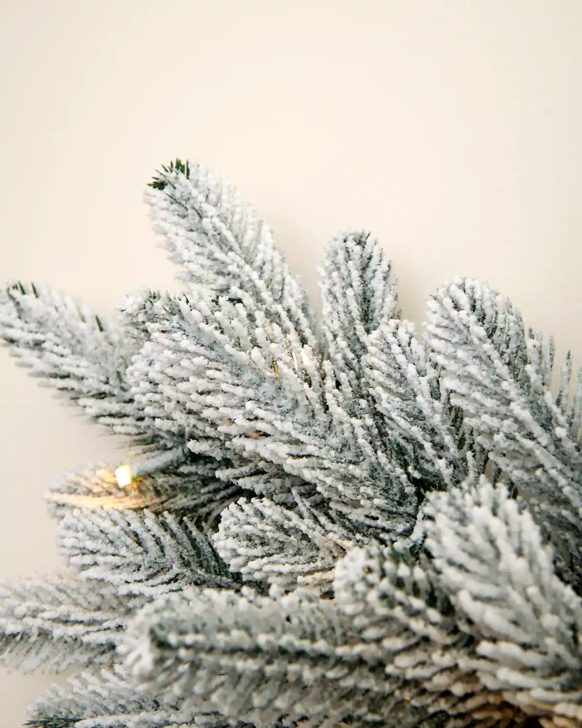 Close-up of the snowflake wreath showing thick snow-flocked foliage with warm white LED lights between the branches.