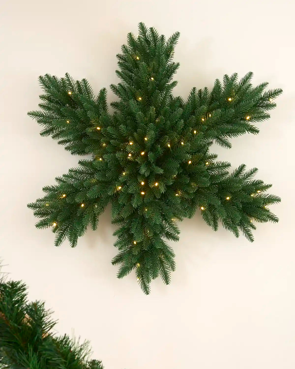 Pre-lit 80 cm snowflake wreath with green foliage and warm white LED lights displayed on a wall.