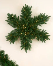 Pre-lit 80 cm snowflake wreath with green foliage and warm white LED lights displayed on a wall.