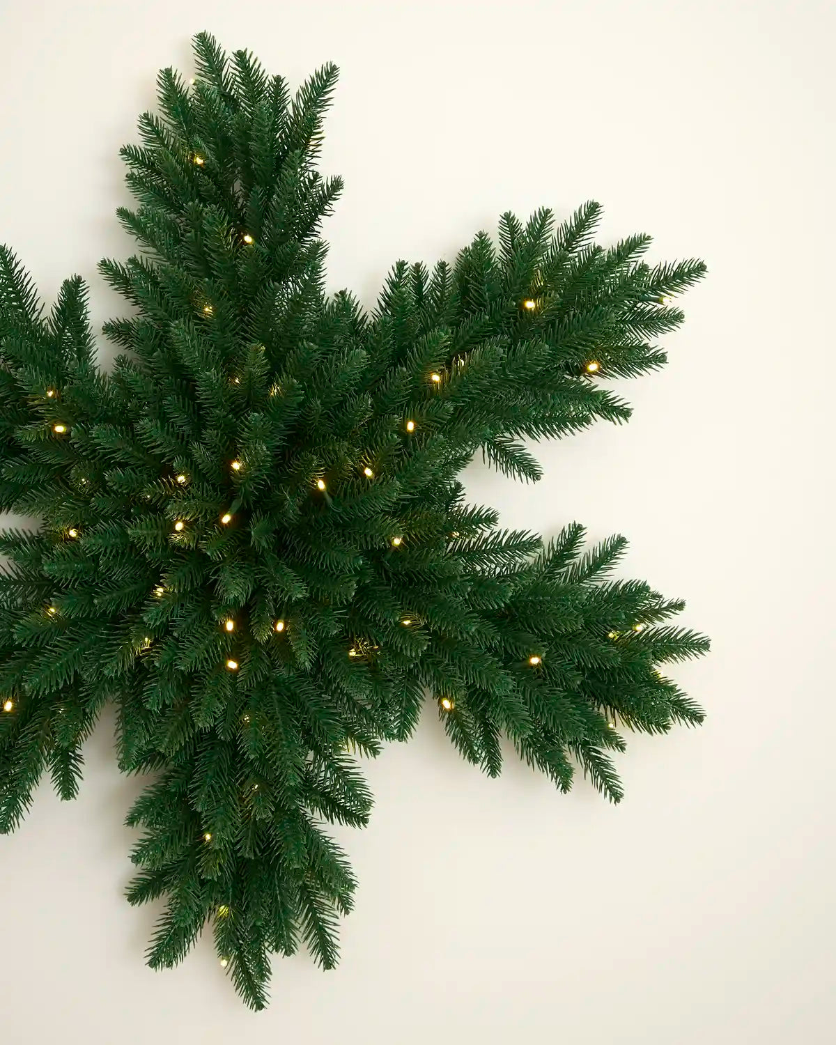 Close view of the green snowflake wreath showing its full foliage and warm white LED lights.
