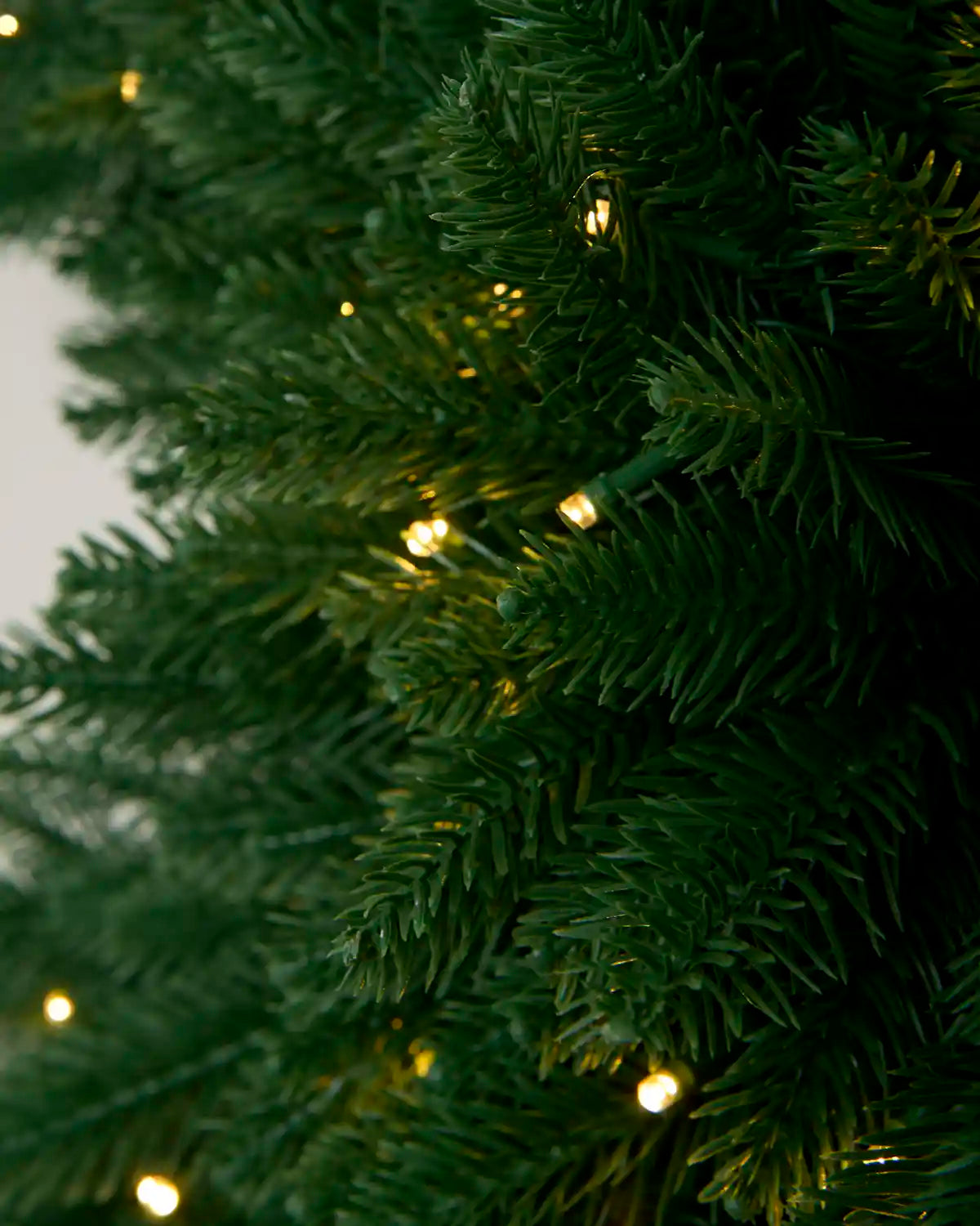 Close-up of warm white LED lights illuminated among the dense green foliage of the snowflake wreath.