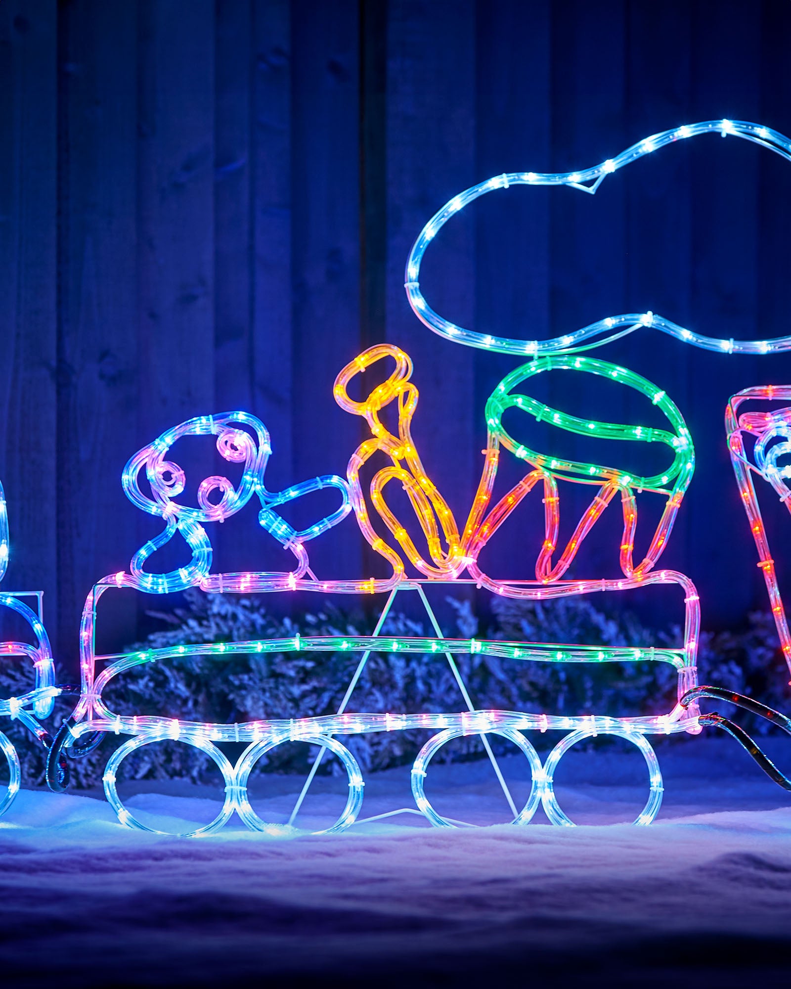 Close-up of the train carriage with a drum, teddy bear and trumpet outlined in multi-coloured lights